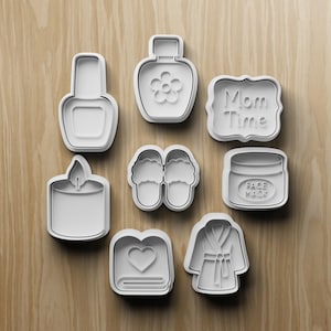Peut inclure: Ensemble de découpoirs à biscuits en plastique blanc représentant un flacon de vernis à ongles, une bouteille avec une fleur, une pancarte "Mom Time", une bougie, une paire de pantoufles, un pot de masque facial, un livre avec un cœur et un peignoir.