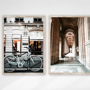 May include: Two framed photographs of Paris. The left photo shows a white bicycle parked in front of a building with the word "Chanel" on the storefront. The right photo shows a long, arched hallway with a tiled floor.