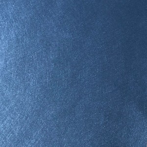 May include: A close-up shot of a textured, solid blue surface. The surface has a subtle, shimmering effect, with visible fine lines and a slightly uneven texture. The color is a deep, saturated blue.