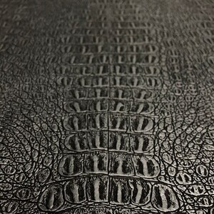 K&ouml;nnte beinhalten: Schwarze, krokodilgepr&auml;gte Ledertextur mit einem sich wiederholenden Schuppenmuster.