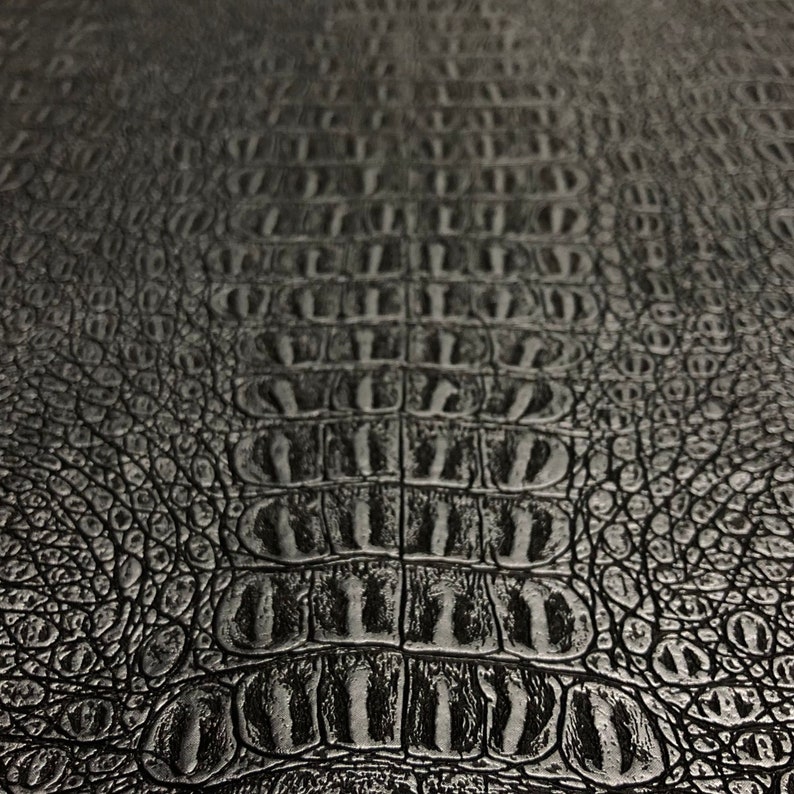 K&ouml;nnte beinhalten: Schwarze, krokodilgepr&auml;gte Ledertextur mit einem sich wiederholenden Schuppenmuster.