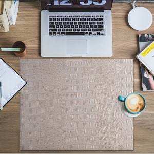 K&ouml;nnte beinhalten: Eine hellbraune Schreibtischmatte aus Kunstleder mit Krokodil-Muster. Die Matte liegt auf einem Holztisch mit einem Laptop, einem Notizbuch, einer Kaffeetasse und einem Magazin.