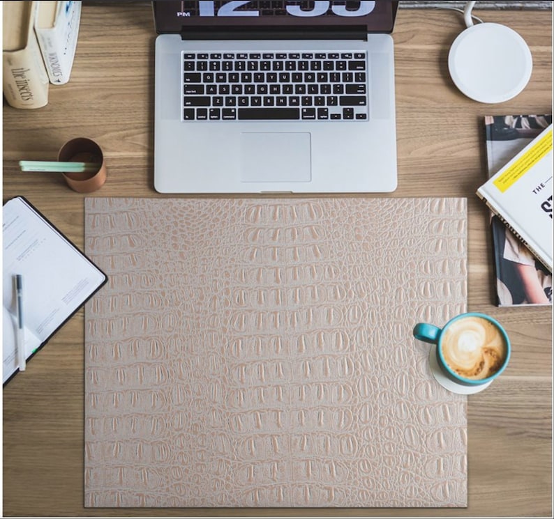 K&ouml;nnte beinhalten: Eine hellbraune Schreibtischmatte aus Kunstleder mit Krokodil-Muster. Die Matte liegt auf einem Holztisch mit einem Laptop, einem Notizbuch, einer Kaffeetasse und einem Magazin.