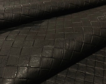 Könnte beinhalten: Schwarzes Leder mit einem gewebten quadratischen Muster. Das Leder ist in der Mitte gefaltet und zeigt die Textur des Materials.