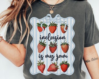 May include: Dark gray t-shirt featuring a blue and white striped frame with illustrations of strawberries. The text "inclusion is my jam" is displayed within the frame. The shirt is made of a soft material.
