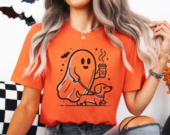 May include: Orange t-shirt with a ghost holding a coffee cup and walking a dachshund. The ghost has a friendly face and the dachshund is looking to the right. The shirt has a black and white design.