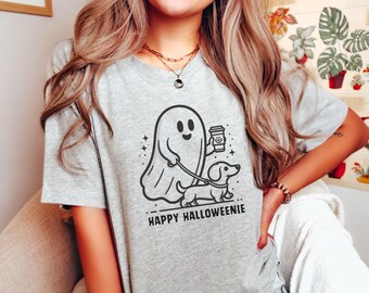 May include: A gray t-shirt with a black and white illustration of a ghost holding a coffee cup and walking a dachshund. The text "Happy Halloweenie" is printed below the illustration.