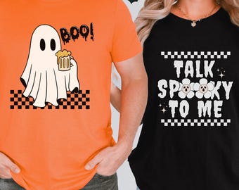 May include: Two t-shirts with a Halloween theme. The orange t-shirt has a ghost holding a beer with the text "BOO!" The black t-shirt has the text "TALK SPOOKY TO ME" with two ghost faces in flowers.