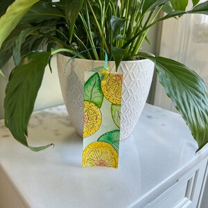 May include: A watercolor bookmark with a lemon theme. The bookmark features yellow lemons with green leaves on a white background.