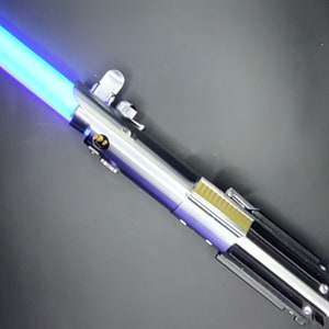 May include: A blue lightsaber with a silver and black handle. The lightsaber is lit and the blade is a bright blue color.