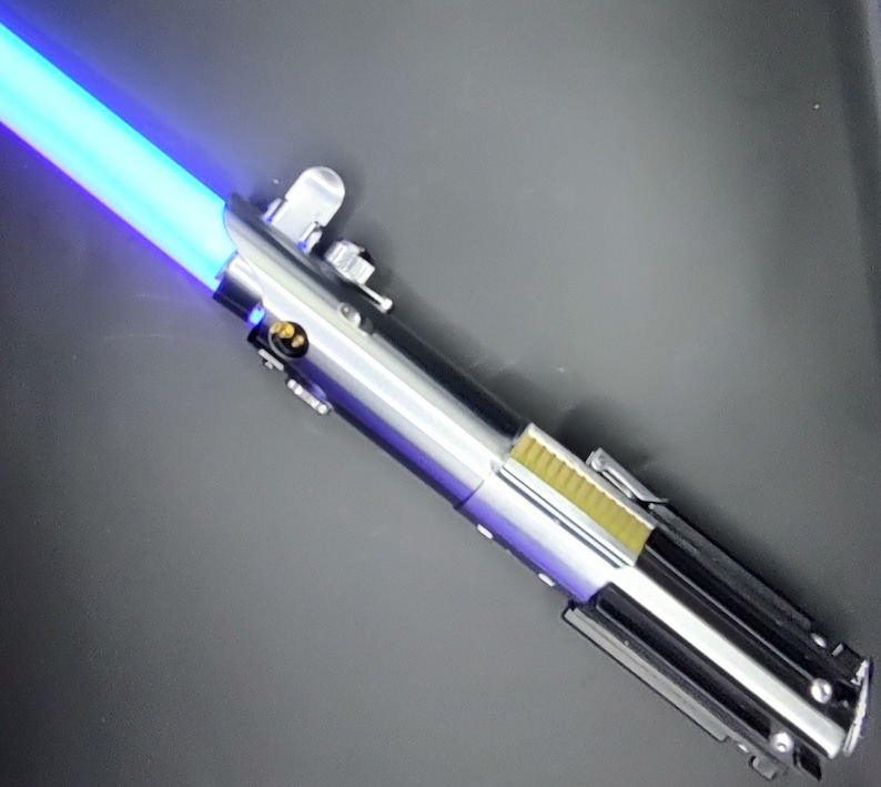 May include: A blue lightsaber with a silver and black handle. The lightsaber is lit and the blade is a bright blue color.