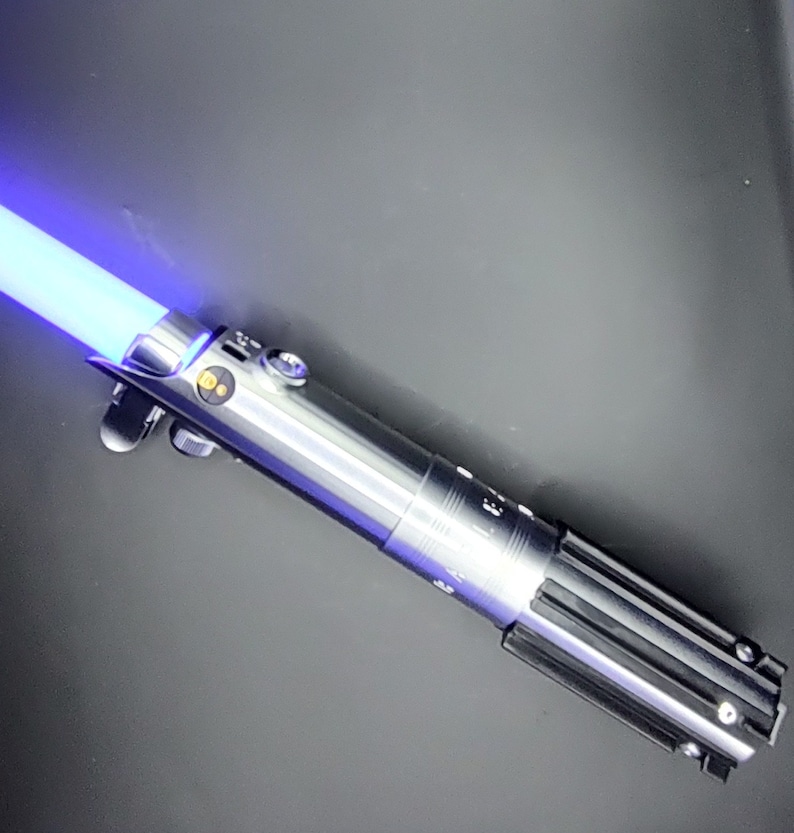 May include: A silver and black lightsaber with a blue blade. The lightsaber has a textured silver handle and a black grip.