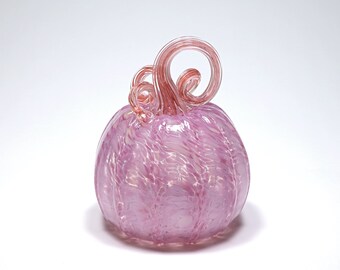Può includere: Una zucca di vetro rosa con un design a spirale e uno stelo rosso. La zucca è fatta di vetro e ha una finitura lucida.