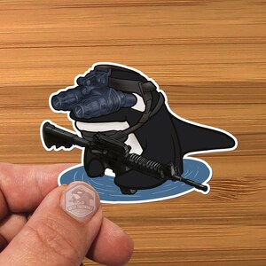 May include: A black and white cartoon orca wearing a black tactical helmet with night vision goggles and holding a black rifle. The orca is swimming in blue water.