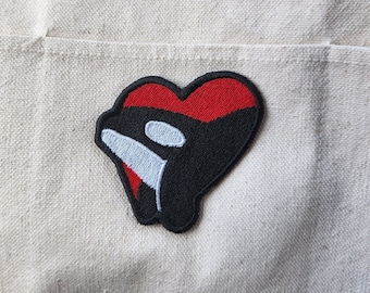 Peut inclure: Écusson brodé représentant une orque noire dans un cœur rouge. L'orque a un œil blanc et une bande blanche. L'écusson est sur un fond de tissu beige. Convient aux vestes, sacs ou autres articles en tissu.