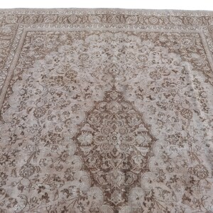 Peut inclure: Un tapis vintage avec un fond beige et un motif floral brun. Le tapis a un m&eacute;daillon central et une bordure avec un motif r&eacute;p&eacute;titif.