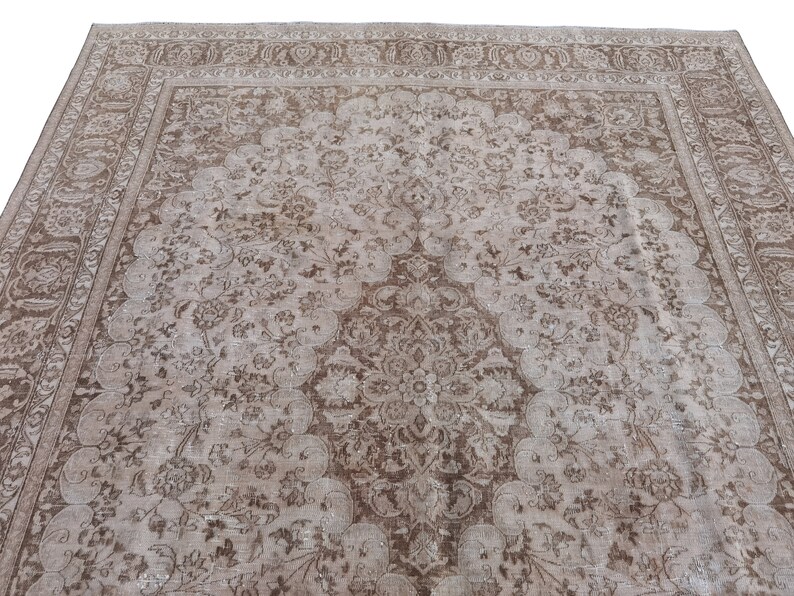 Peut inclure: Un tapis vintage avec un fond beige et un motif floral brun. Le tapis a un m&eacute;daillon central et une bordure avec un motif r&eacute;p&eacute;titif.