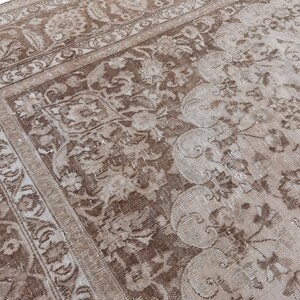 Peut inclure: Un tapis vintage avec un motif floral d&eacute;lav&eacute; dans des tons de brun et de blanc. Le tapis a un aspect vieilli et une texture us&eacute;e.