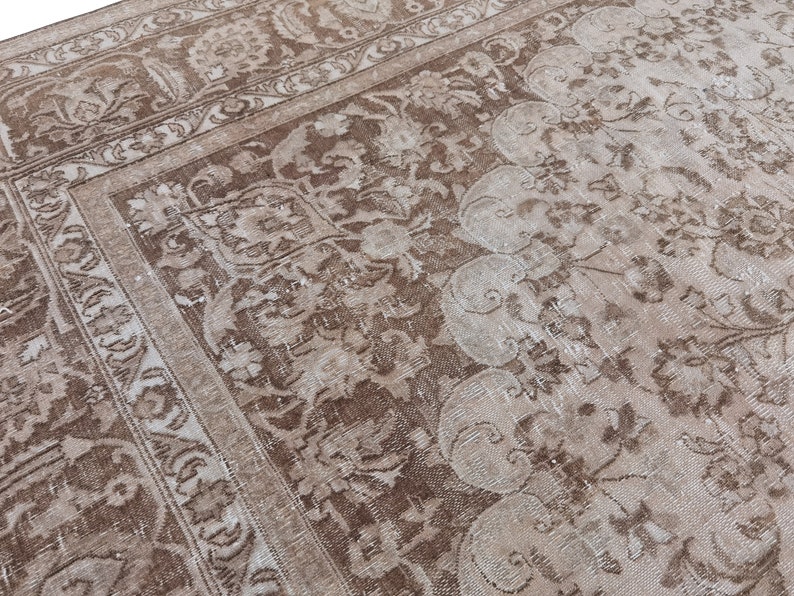 Peut inclure: Un tapis vintage avec un motif floral d&eacute;lav&eacute; dans des tons de brun et de blanc. Le tapis a un aspect vieilli et une texture us&eacute;e.