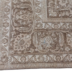 Peut inclure: Un tapis vintage avec un fond beige et un motif floral brun. Le tapis a une bordure &agrave; franges.