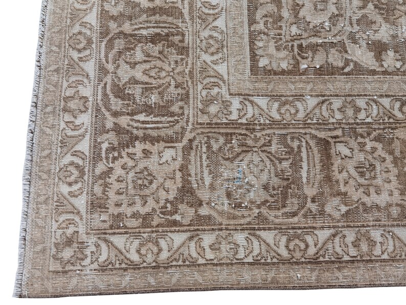 Peut inclure: Un tapis vintage avec un fond beige et un motif floral brun. Le tapis a une bordure &agrave; franges.