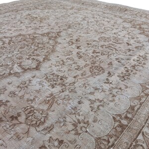 Peut inclure: Un tapis vintage avec un motif floral d&eacute;lav&eacute; dans des tons de brun et de blanc. Le tapis a un aspect vieilli et une texture us&eacute;e.
