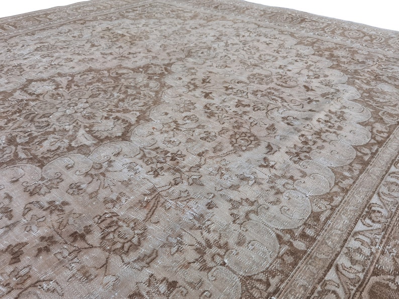 Peut inclure: Un tapis vintage avec un motif floral d&eacute;lav&eacute; dans des tons de brun et de blanc. Le tapis a un aspect vieilli et une texture us&eacute;e.