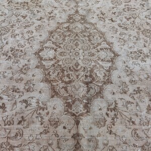 Peut inclure: Un tapis vintage avec un motif floral d&eacute;lav&eacute; dans des tons de brun et beige.