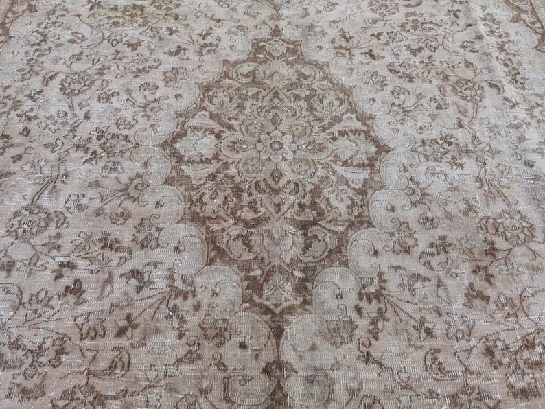 Peut inclure: Un tapis vintage avec un motif floral d&eacute;lav&eacute; dans des tons de brun et beige.
