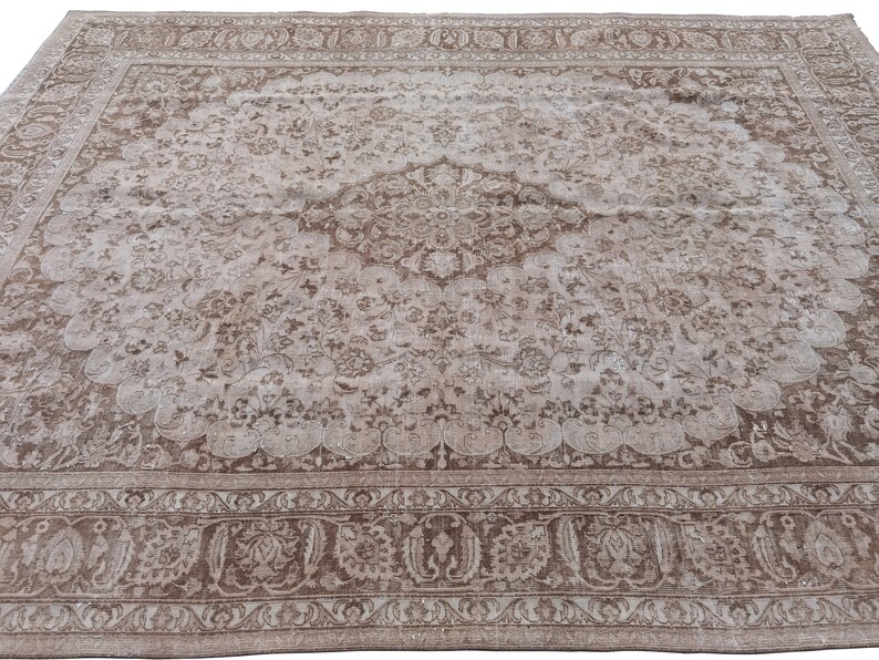 Peut inclure: Un tapis vintage avec un fond brun clair et un motif floral d&eacute;taill&eacute; en brun fonc&eacute;. Le tapis a un m&eacute;daillon central avec un motif r&eacute;p&eacute;titif de fleurs et de feuilles.