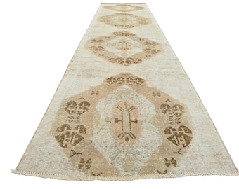 May include: A rectangular, beige runner rug with a distressed, vintage appearance. The rug features repeating geometric patterns in shades of brown and tan. The design includes diamond and floral motifs, creating a classic, aged aesthetic.