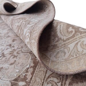 Peut inclure: Un tapis vintage beige et marron avec un motif floral. Le tapis est pli&eacute; en deux et les bords sont visibles.