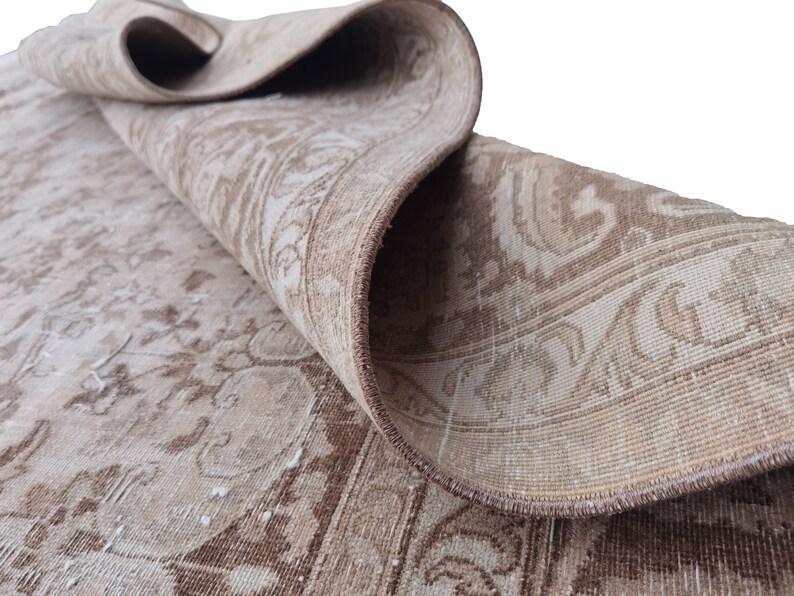 Peut inclure: Un tapis vintage beige et marron avec un motif floral. Le tapis est pli&eacute; en deux et les bords sont visibles.