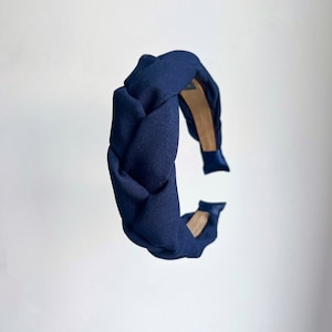 May include: A navy blue braided headband made of fabric. The headband is a simple, elegant design.