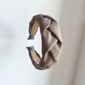 Puede incluir: Una diadema trenzada marrón hecha de tela. La diadema es un diseño simple y elegante.