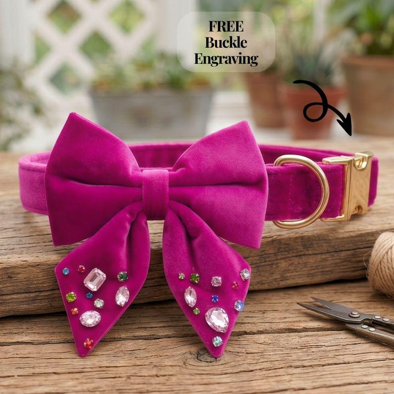 May include: A magenta velvet dog collar with a large bow adorned with colorful rhinestones. The collar has a gold-colored buckle and a D-ring. The image includes the text "FREE Buckle Engraving".