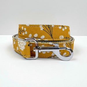 May include: A yellow dog leash with a white floral pattern and a silver clip.