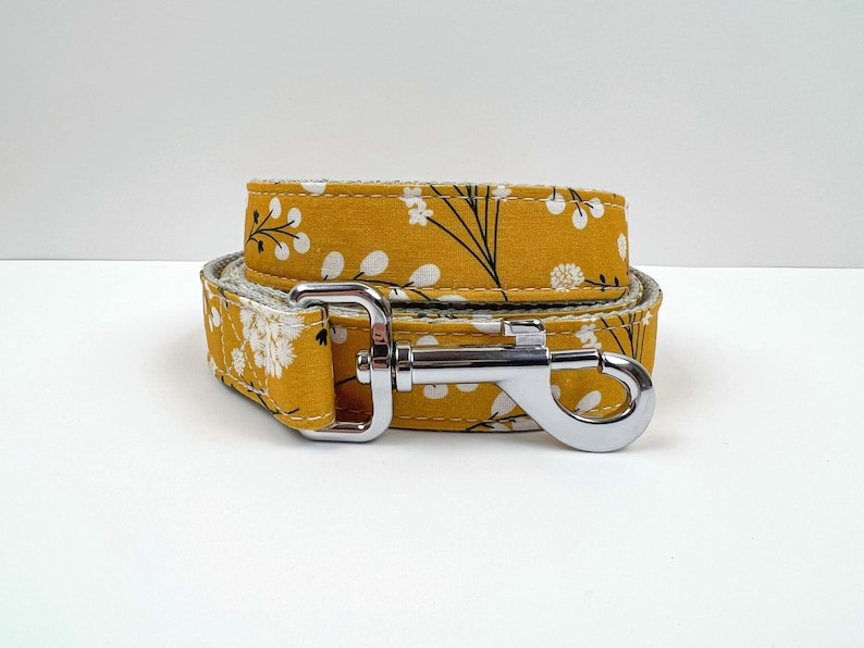 May include: A yellow dog leash with a white floral pattern and a silver clip.