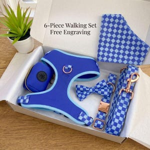 Könnte beinhalten: Ein sechsteiliges Hunde-Walking-Set in einer weißen Box. Das Set enthält ein blaues Geschirr, eine Leine, eine Fliege, ein Halstuch und einen Abfallbeutelspender. Das Set hat ein blaues und hellblaues Karomuster und roségoldfarbene Hardware. Text: "6-Piece Walking Set Free Engraving."