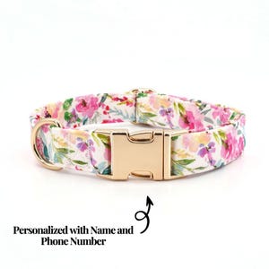 May include: A floral dog collar with a gold-colored buckle and D-ring. The collar features a white background with pink, purple, and yellow flower patterns. The text "Personalized with Name and Phone Number" is also visible.