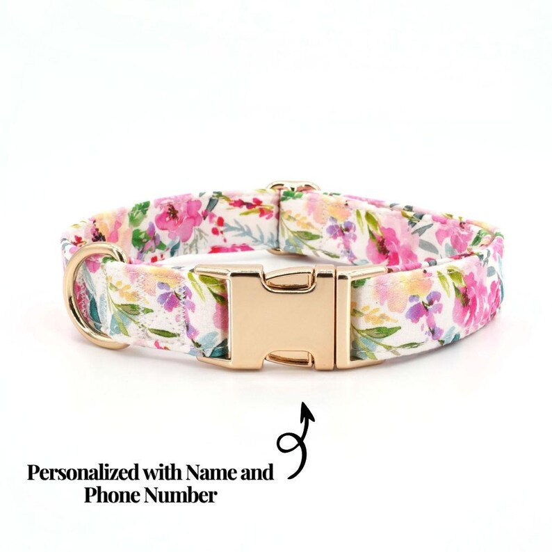 May include: A floral dog collar with a gold-colored buckle and D-ring. The collar features a white background with pink, purple, and yellow flower patterns. The text "Personalized with Name and Phone Number" is also visible.
