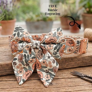 Può includere: Un collare per cani e un papillon abbinato con un motivo floreale. Il tessuto color crema è adornato da fiori arancioni, rosa e grigi. L'hardware metallico è in oro rosa. L'immagine include il testo "FREE Buckle Engraving".