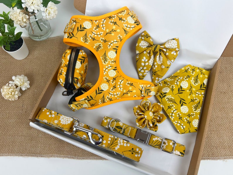May include: A yellow dog harness with a floral pattern, a matching leash, a poop bag holder, a bow tie, a bandana, and a flower-shaped dog collar.