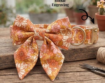 May include: A pet collar featuring a large bow with a floral pattern in shades of orange, pink, and cream. The collar includes a gold-toned metal buckle and a D-ring. Text above the collar reads FREE Buckle Engraving.