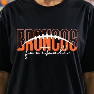 May include: Black t-shirt with the word "BRONCOS" in orange block letters with a white football graphic. The word "football" is written in a cursive font below the football graphic.