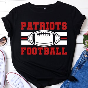 May include: Black t-shirt with the words "PATRIOTS FOOTBALL" in red block letters. A white football graphic is centered between the words, with a red stripe above and below it. The shirt is a casual style.