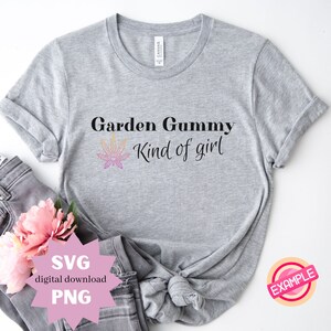 Può includere: Maglietta grigia con il testo "Garden Gummy Kind of girl" e una grafica di foglia di marijuana rosa e gialla. La maglietta è su una superficie bianca con un paio di jeans e un fiore rosa.