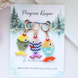 May include: Three beaded fish progress keepers in yellow, green, blue, and pink, with gold-coloured clasps. The card reads "Progress Keeper" and "for knitters with love" with a website address.