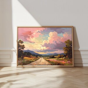 May include: A framed landscape painting showing a road winding towards mountains beneath a colourful sky. The artwork uses pink, yellow, and purple tones, with trees and fields in the foreground. The painting is presented in a wooden frame.