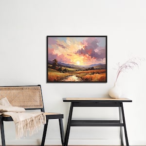 May include: A framed landscape painting depicts a sunset over a valley with a river. The sky is filled with pink, orange, and purple clouds. The foreground features golden fields and green hills.